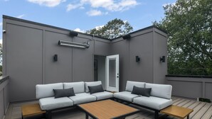 A modern outdoor seating area with a grey wall, a white sectional sofa, and a wooden coffee table. - Modern Home with Rooftop Deck (Atlanta)