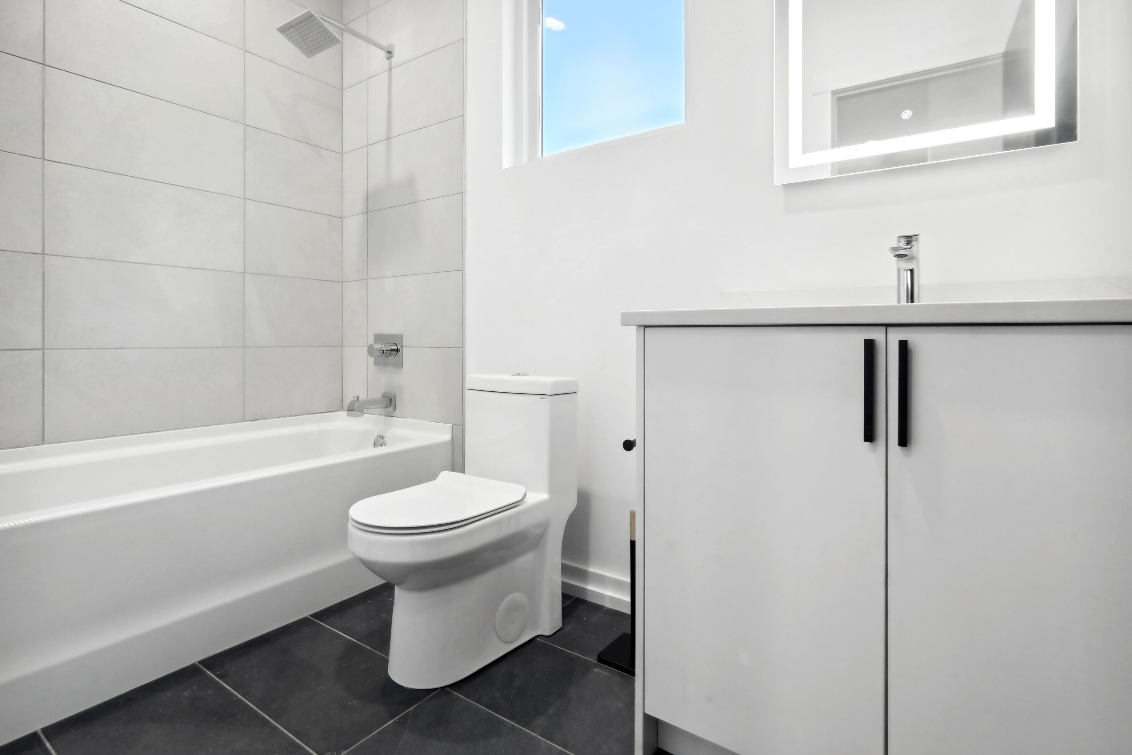 A modern bathroom with a bathtub, toilet, and a cabinet.