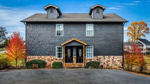 A two-story house with a stone foundation, a black front door with a wooden frame, and two chimneys on the roof.