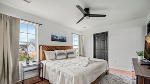 A bedroom with a bed, a desk, a ceiling fan, a door, and a window. - Cozy Hideaway • Hot Tub • Arcade Machine • Dogs OK (Sevierville)