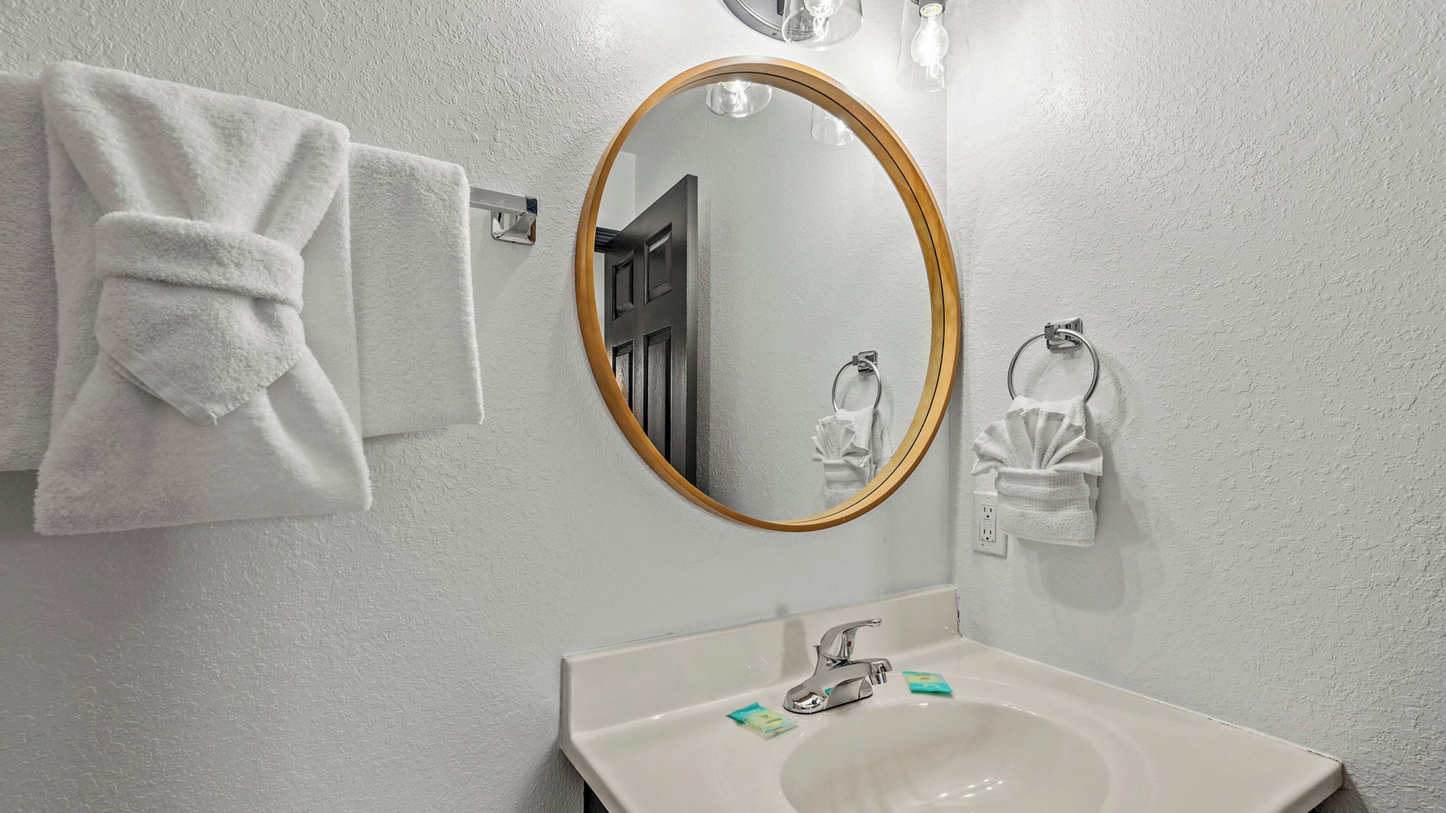 A bathroom with a white sink, a round mirror with a wooden frame, and two white towels hanging on towel rings.