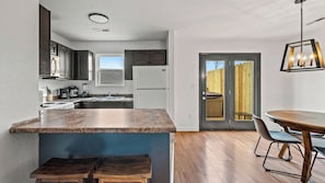 A modern kitchen with granite countertops, a built-in oven, and a dining area with a wooden table and chairs.