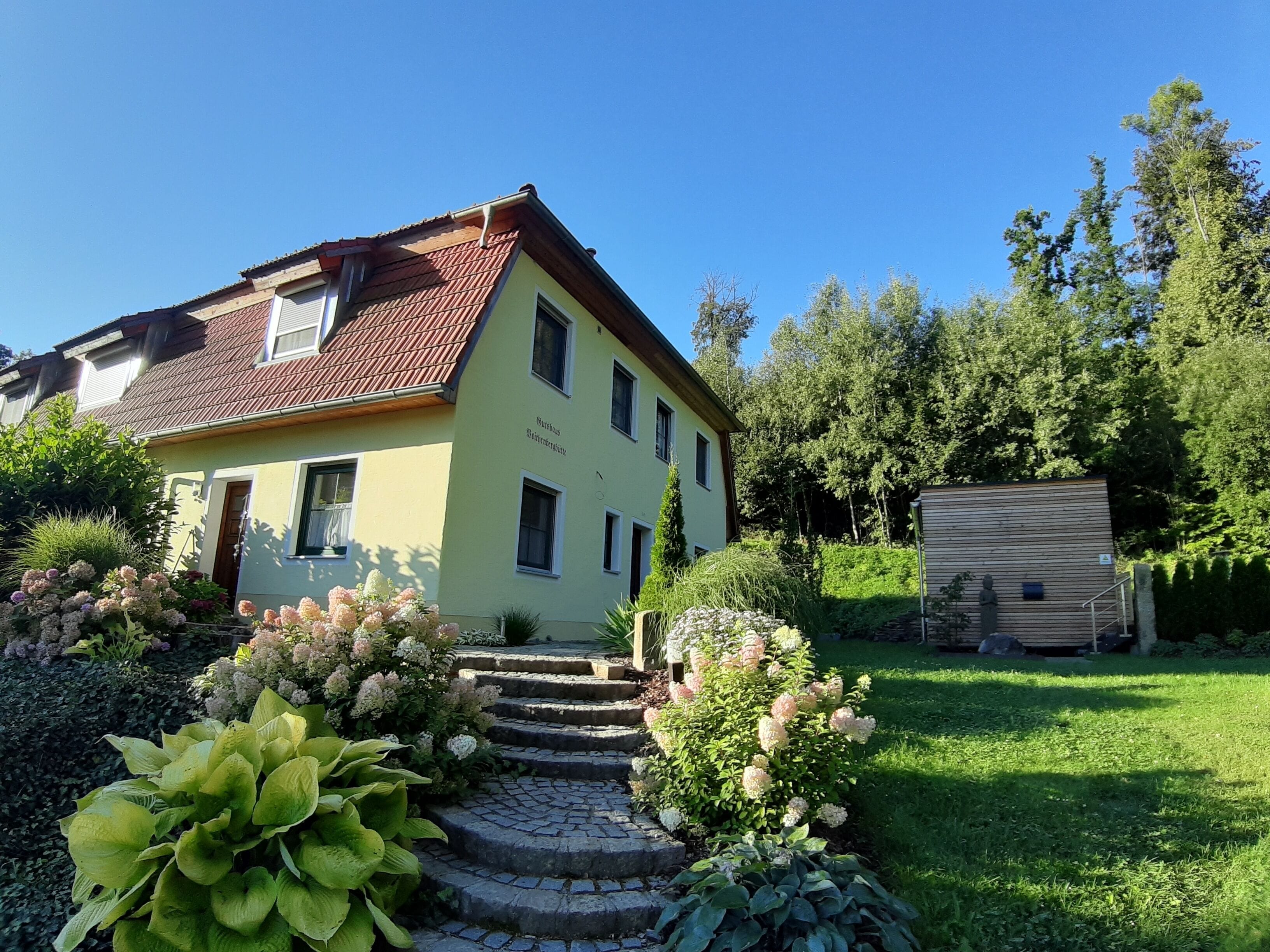 A two-story house with a red-tiled roof, a front garden with stepping stones, and a small wooden shed.