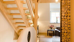 A wooden staircase leading to an upper level, a hanging light fixture, and a wall with stacked logs. - Gutshaus Voithenberghütte right on the edge of the forest with wellness area dog-friendly (Furth im Wald)