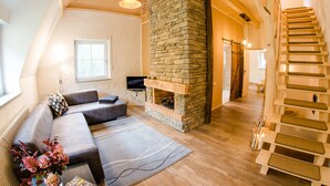 A modern living room with a stone fireplace, a wooden staircase, and a sofa. - Gutshaus Voithenberghütte right on the edge of the forest with wellness area dog-friendly (Furth im Wald)