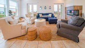 Un salon spacieux comprenant un grand canapé, une table basse et une cheminée. Trois œuvres d’art encadrées ornent le mur, et un téléviseur est fixé au-dessus de la cheminée.