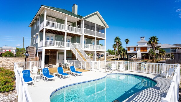 Une maison de deux étages située en bord de mer, dotée d’une piscine et de chaises longues.