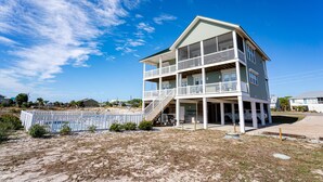 Une maison à deux étages située en bord de mer, dotée d’un balcon, d’une véranda et d’une plage de sable en premier plan.
