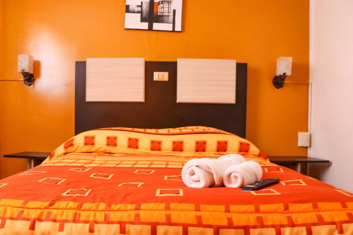 Ein Hotelzimmer mit einem Bett, zwei Nachttischen, einem Kopfteil und einer Wandleuchte.