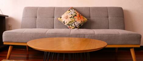 A grey sofa with a floral pillow, a wooden coffee table, and a patterned rug.