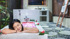A person relaxing in a bathtub filled with water and surrounded by flowers. - The Meranggi (Ubud)