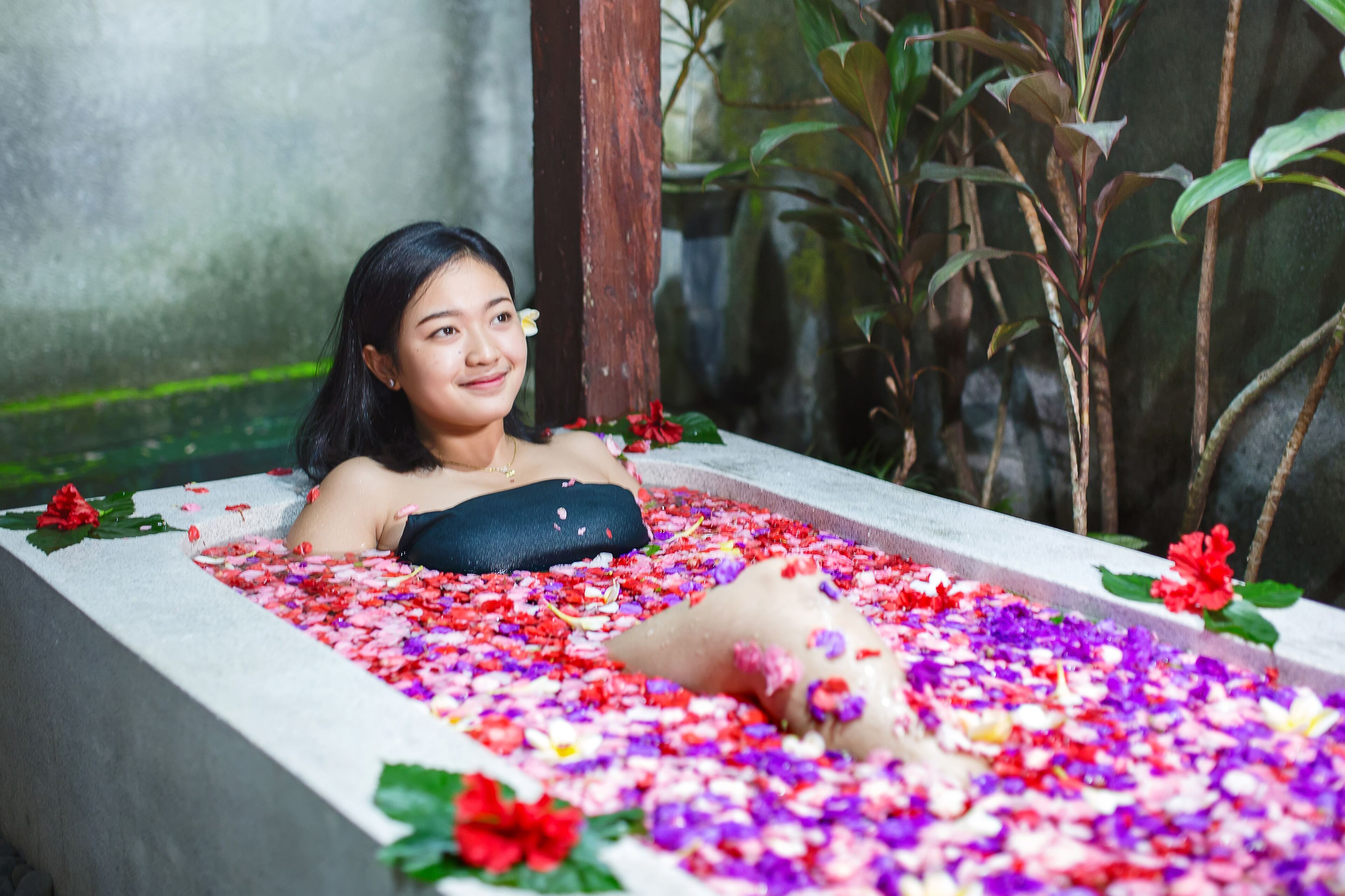 A person relaxing in a bathtub filled with flower petals.