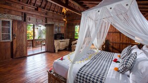 A wooden room with a bed under a canopy, a wooden dresser, and a television. - The Meranggi (Ubud)