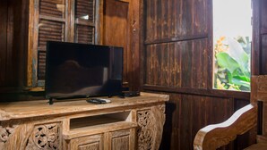 A wooden TV stand with a flat-screen TV, remote controls, and a decorative cabinet. - The Meranggi (Ubud)
