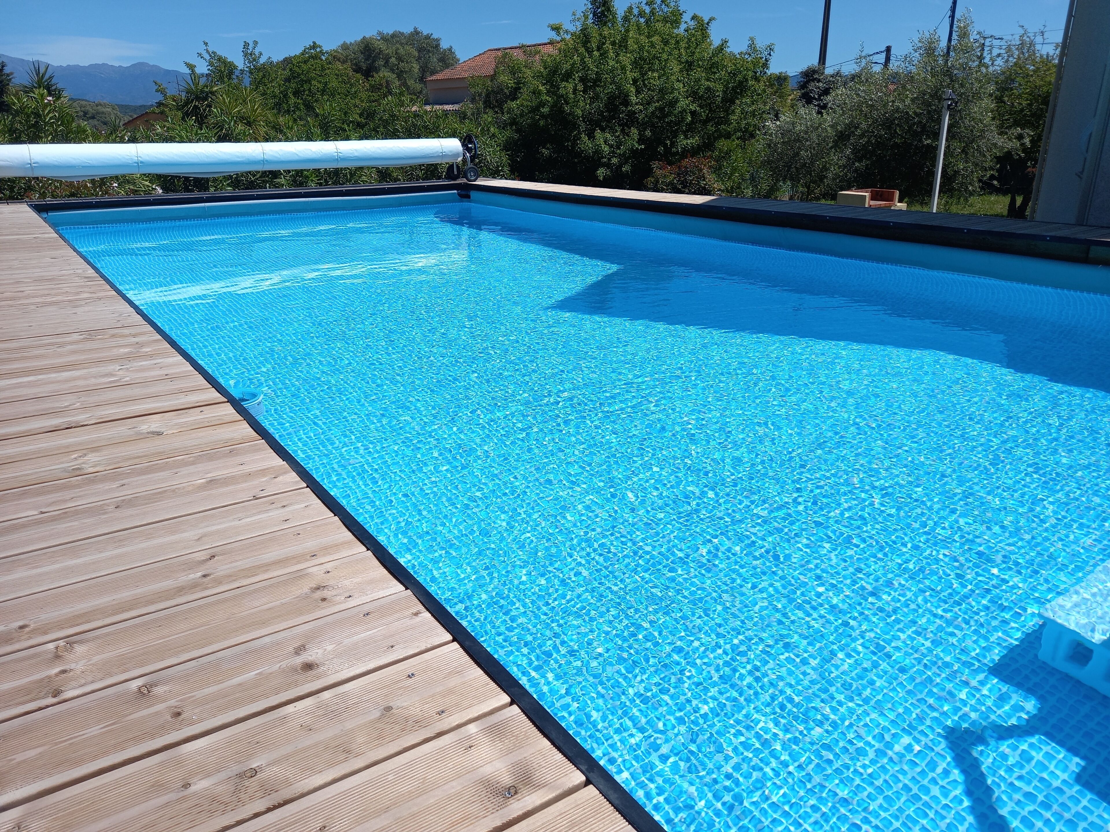A rectangular swimming pool with clear blue water, surrounded by a wooden deck.