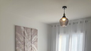 Ein Schlafzimmer mit einem großen Bett, zwei Nachttischlampen, einer Deckenleuchte, einem Fenster mit transparenten Vorhängen und einem Wandbild.
