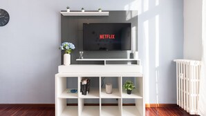 Een moderne woonkamer met een witte tv-meubel, een flatscreen-televisie waarop 'NETFLIX' staat en een radiator aan de rechterkant.