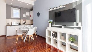Een moderne keuken met witte kasten, een eethoek met een ronde tafel en stoelen, en een inbouwkast voor de televisie.