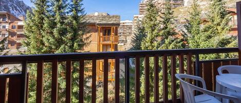 A balcony with a wooden railing, overlooking a mountainous area with buildings and trees.