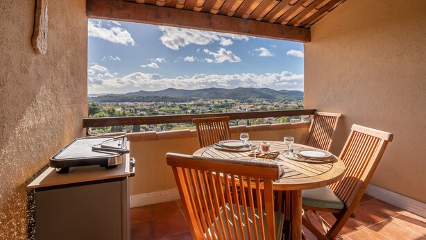 Un balcón con una mesa dispuesta para cuatro personas, con vistas a un paisaje pintoresco.