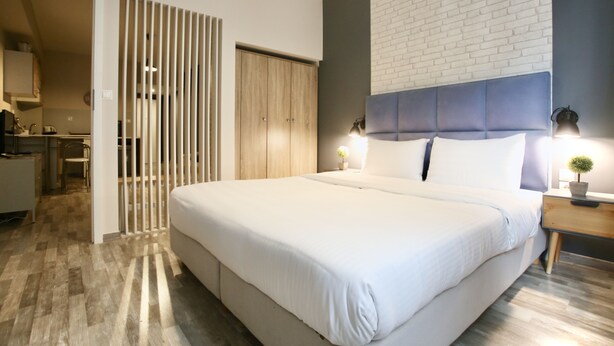 Un dormitorio moderno con una cama grande, un armario de madera, una pared decorativa de ladrillo blanco y una mesita de noche con lámpara.
