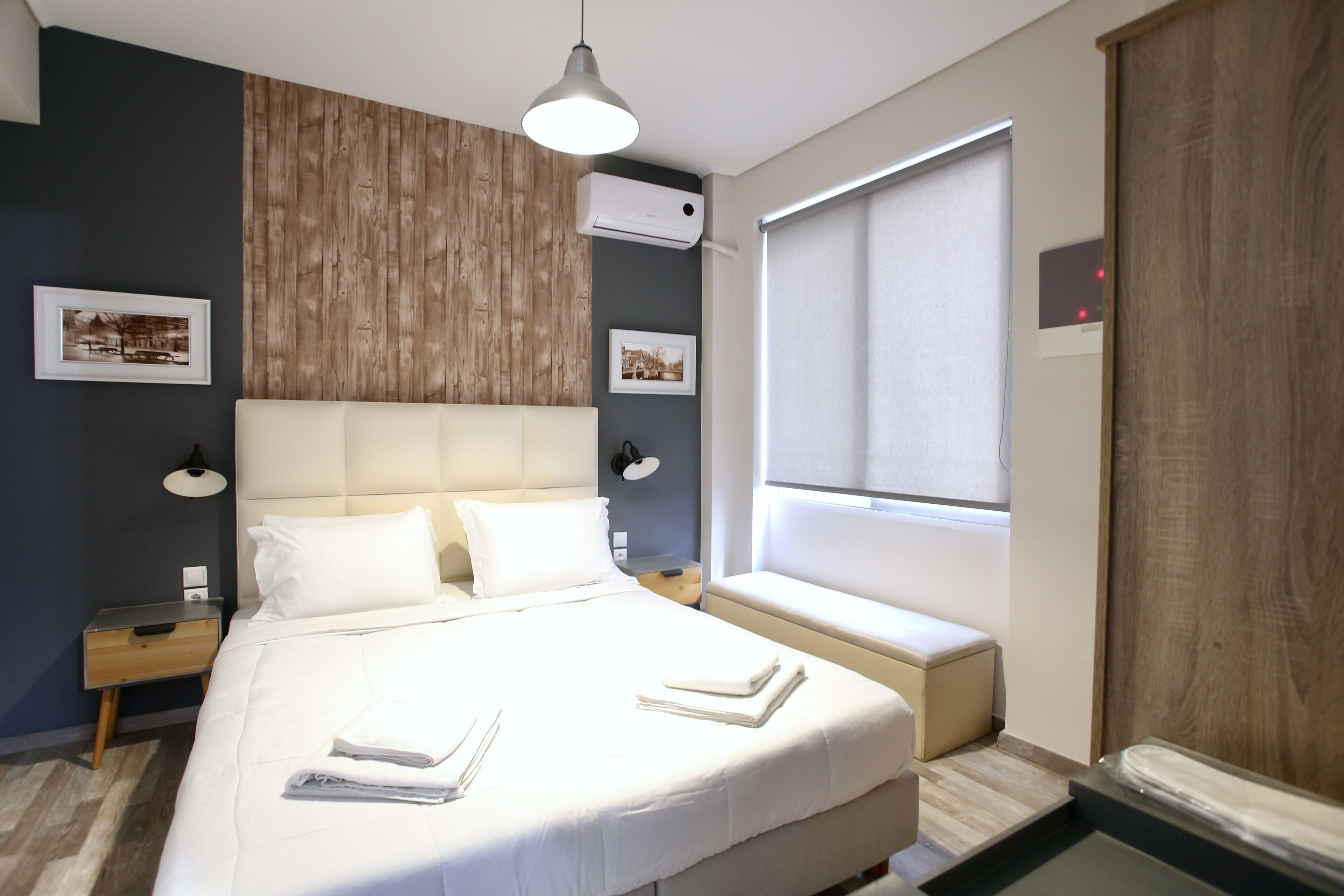 A modern hotel room with a large bed, bedside tables, a wall-mounted air conditioner, and a window with a view.