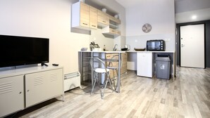 Cocina compacta con televisión, microondas, fregadero y refrigerador. Hay dos sillas y una pequeña mesa de comedor.