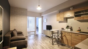Una sala moderna con sofá, comedor con mesa y sillas, cocina con armarios de madera y televisor sobre un mueble.