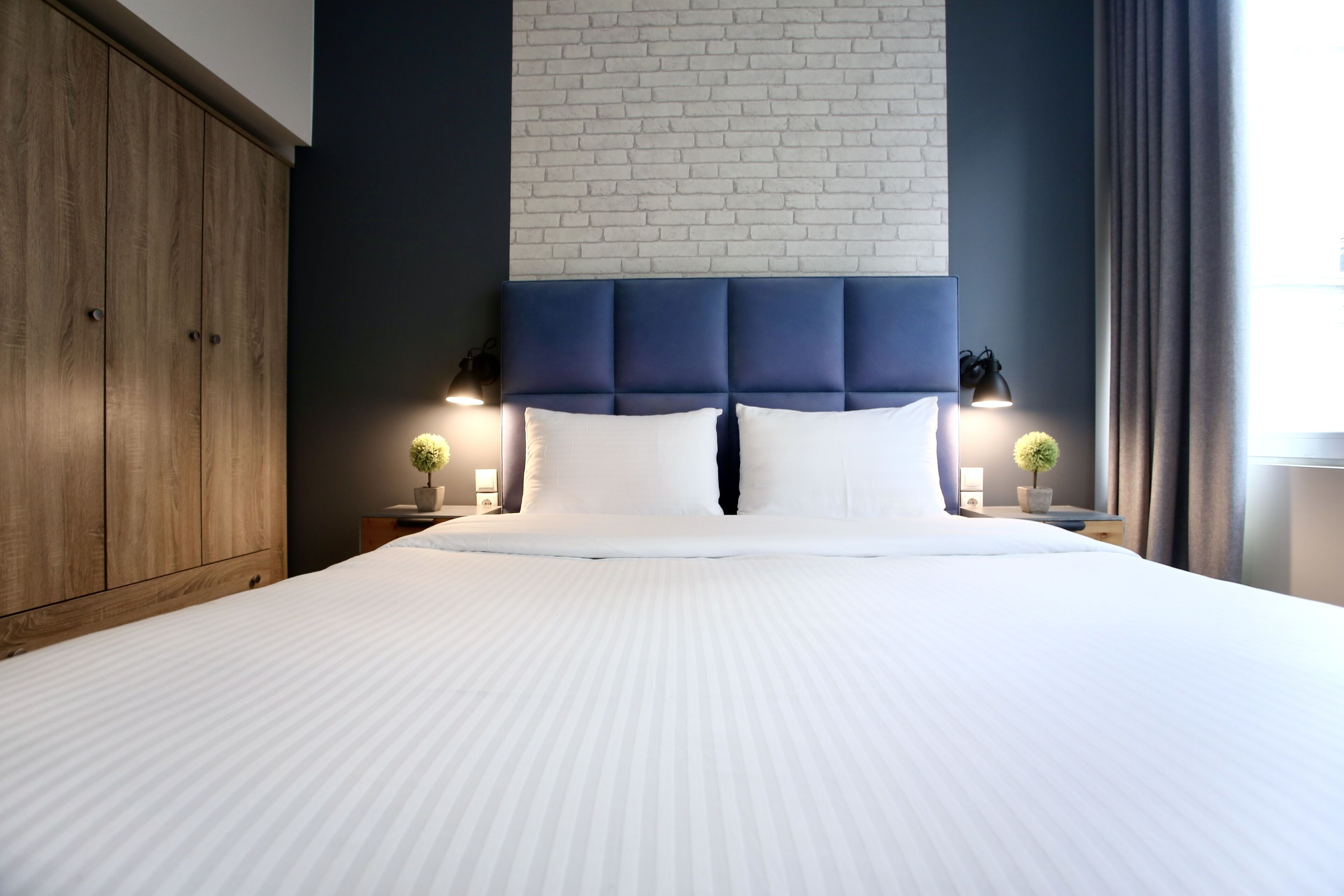 Una cama bien hecha con cabecera azul, dos lámparas de noche y un armario de madera.