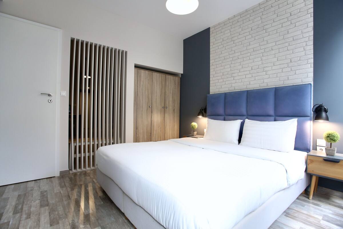 Un dormitorio moderno con una cama grande, un armario, una mesita de noche con lámpara y una pared con diseño de ladrillo.
