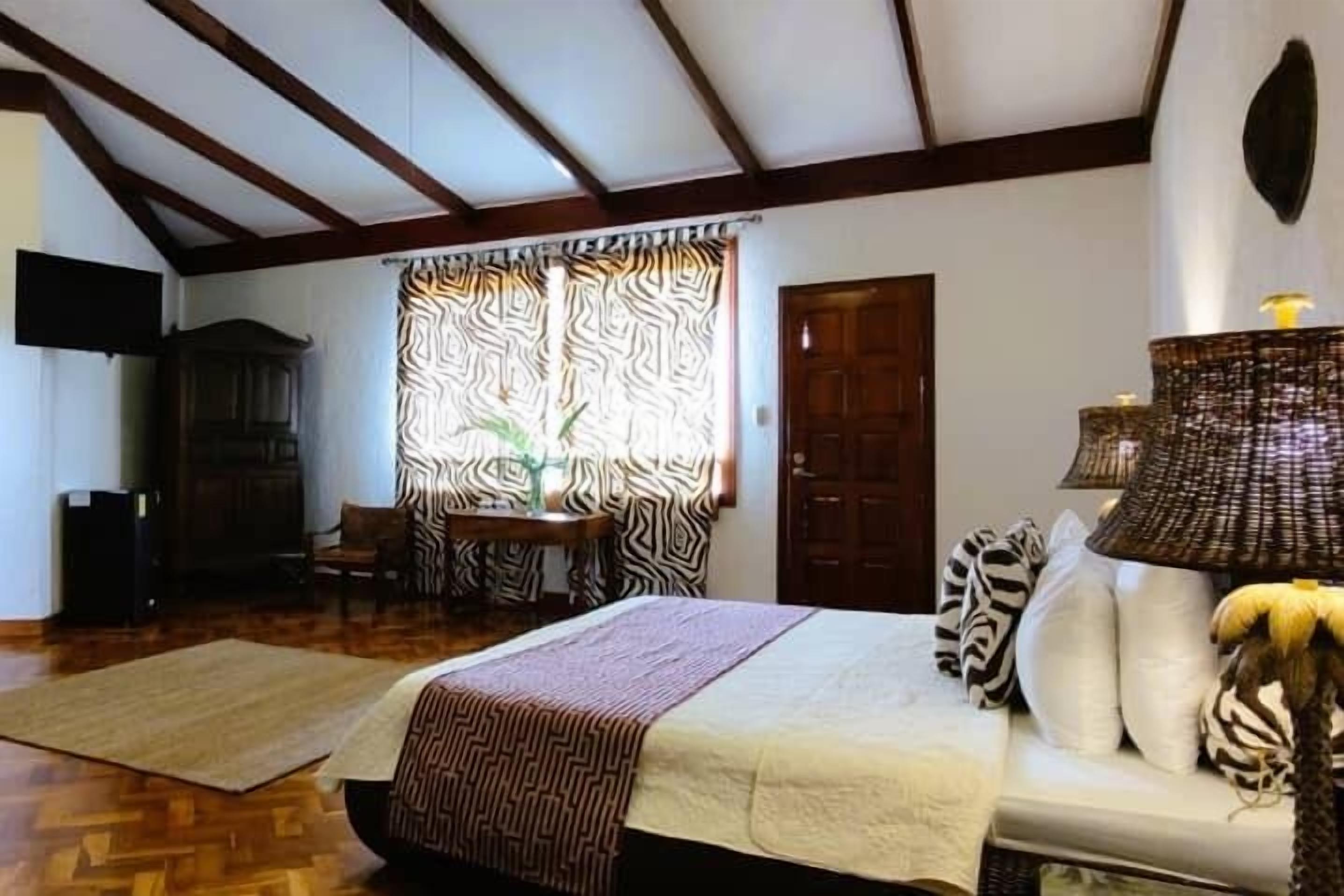 Ein Schlafzimmer mit einem Bett, einem Holzschrank, einem Stuhl, einem gemusterten Vorhang und einer Lampe.