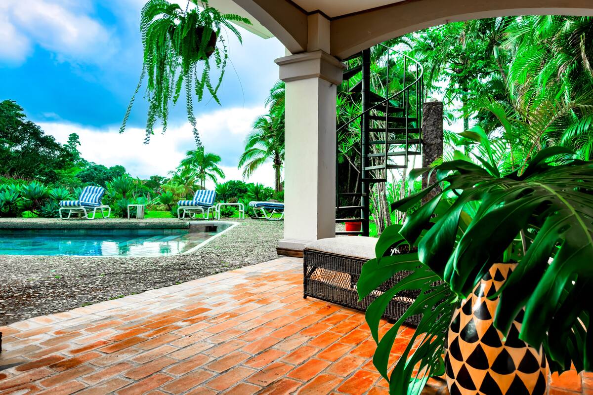 A pool area with lounge chairs, a brick patio, and lush greenery.