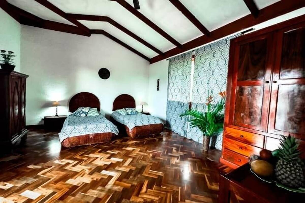 A room with two beds, wooden flooring, a large wardrobe, and patterned wallpaper.