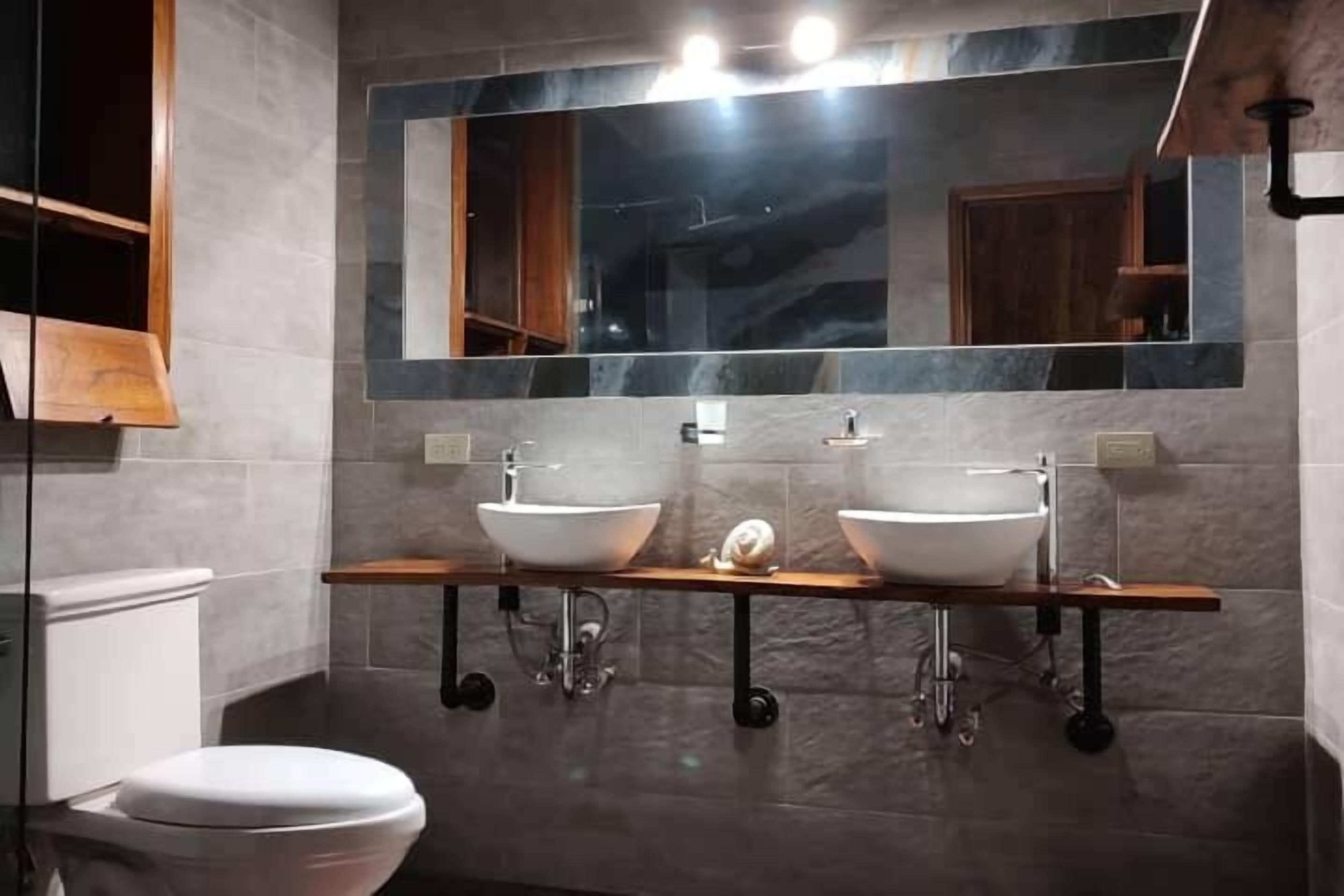 A modern bathroom with two sinks, a large mirror, and a wooden shelf.