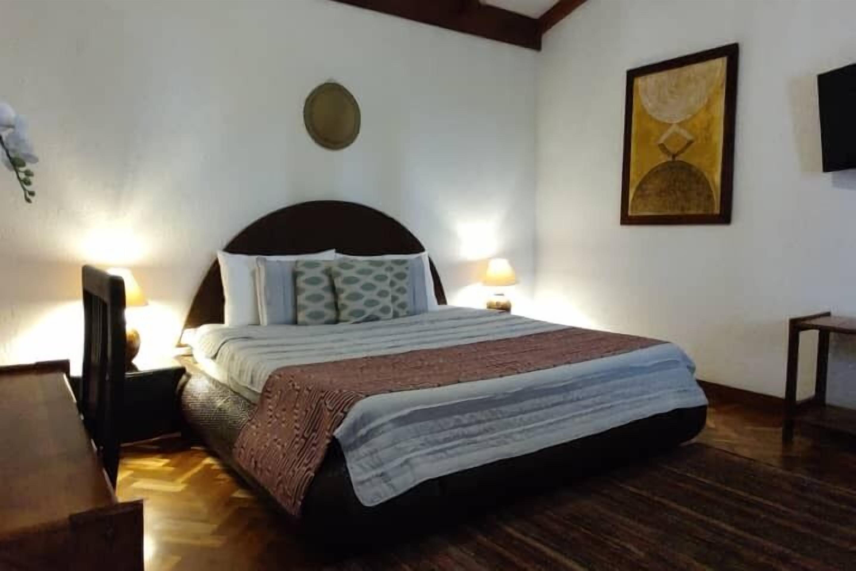 A bedroom with a bed, two bedside tables, a nightstand, a wall clock, and a painting.