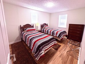 Un dormitorio con dos camas, un aparador de madera, una lámpara y una alfombra.