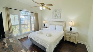 A bedroom with a large bed, two bedside tables, a ceiling fan, and a window with curtains. - Beautiful, Spacious condo in the center of MB (Myrtle Beach)