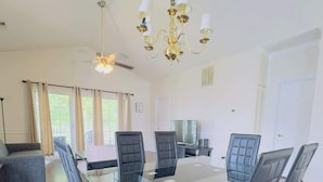 A spacious dining area with a glass table, black cushioned chairs, a chandelier, and a ceiling fan. - Beautiful, Spacious condo in the center of MB (Myrtle Beach)