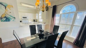A dining area with a glass table, black chairs, a chandelier, and a view of the kitchen. - Beautiful, Spacious condo in the center of MB (Myrtle Beach)