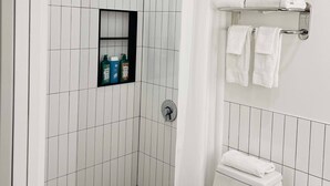 A modern bathroom with a shower, toilet, and a shelf with toiletries. - Bardo Lofts Courtyard Suite #102 (Dallas)