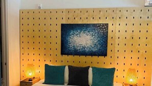 A neatly made bed with a wooden headboard, two bedside lamps, and a large abstract painting above the bed. - Bardo Lofts Courtyard Suite #102 (Dallas)