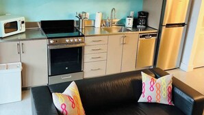 A compact kitchen with a microwave, stove, oven, and refrigerator. There is a black leather sofa with colorful cushions. - Bardo Lofts Courtyard Suite #102 (Dallas)