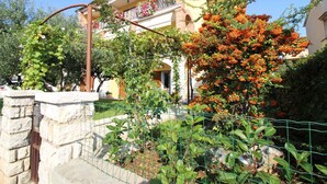 A house with a balcony, surrounded by greenery and a stone wall. - Holiday apartment with barbecue and air conditioning (Poreč)