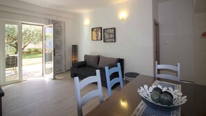 A modern living room with a sofa, dining table, and chairs. There is a sliding glass door leading to a patio area. - Holiday apartment with barbecue and air conditioning (Poreč)