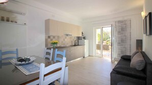 A modern kitchen with white cabinets, a dining table with chairs, and a sofa in a living area with a sliding glass door leading to an outdoor patio. - Holiday apartment with barbecue and air conditioning (Poreč)