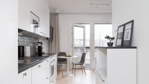 A modern kitchen with white cabinets, a dining table with chairs, and a view of the city through large windows. - Rahulihomes Jyväskylä (Jyväskylä)