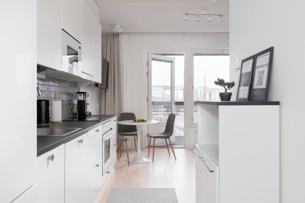 A modern kitchen with white cabinets, a dining table with chairs, and a view of the city through large windows.