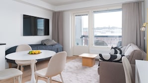 A modern living room with a sofa, a dining table with chairs, a flat-screen TV mounted on the wall, and a large window with curtains. - Rahulihomes Jyväskylä (Jyväskylä)