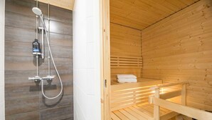 A sauna with a wooden bench, a shower area with a handheld showerhead, and a towel on the bench. - Rahulihomes Jyväskylä (Jyväskylä)