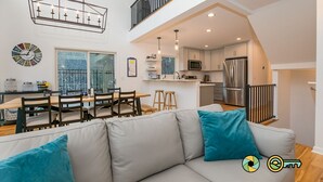 Eine moderne Küche mit Edelstahlgeräten, ein Essbereich mit Holzmöbeln und ein Wohnbereich im Loft-Stil mit Sofa und Kissen.